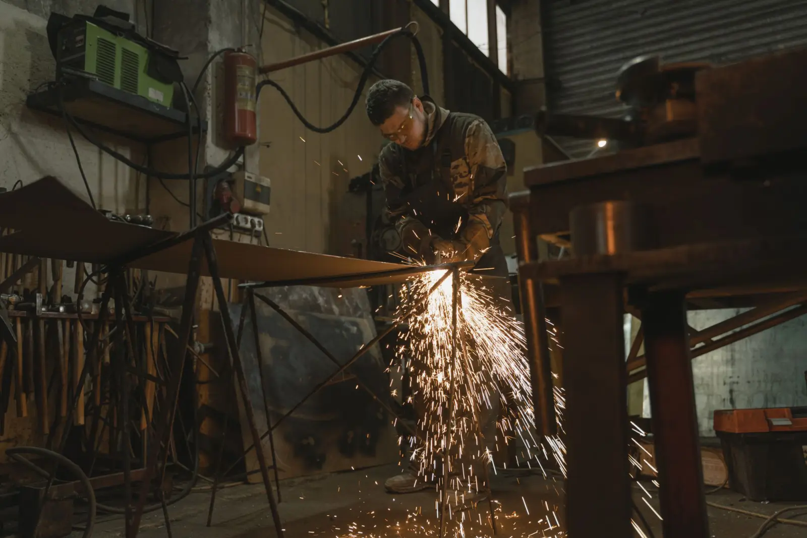 A fabricator cutting steel stock in a metal shop, sparks streaming from the cut
