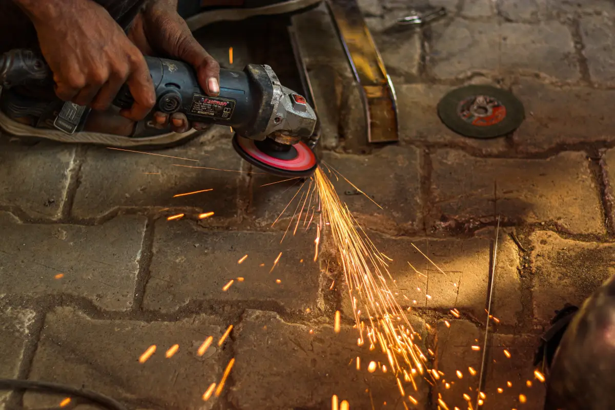 An angle grinder cutting through steel with sparks fanning across the ground
