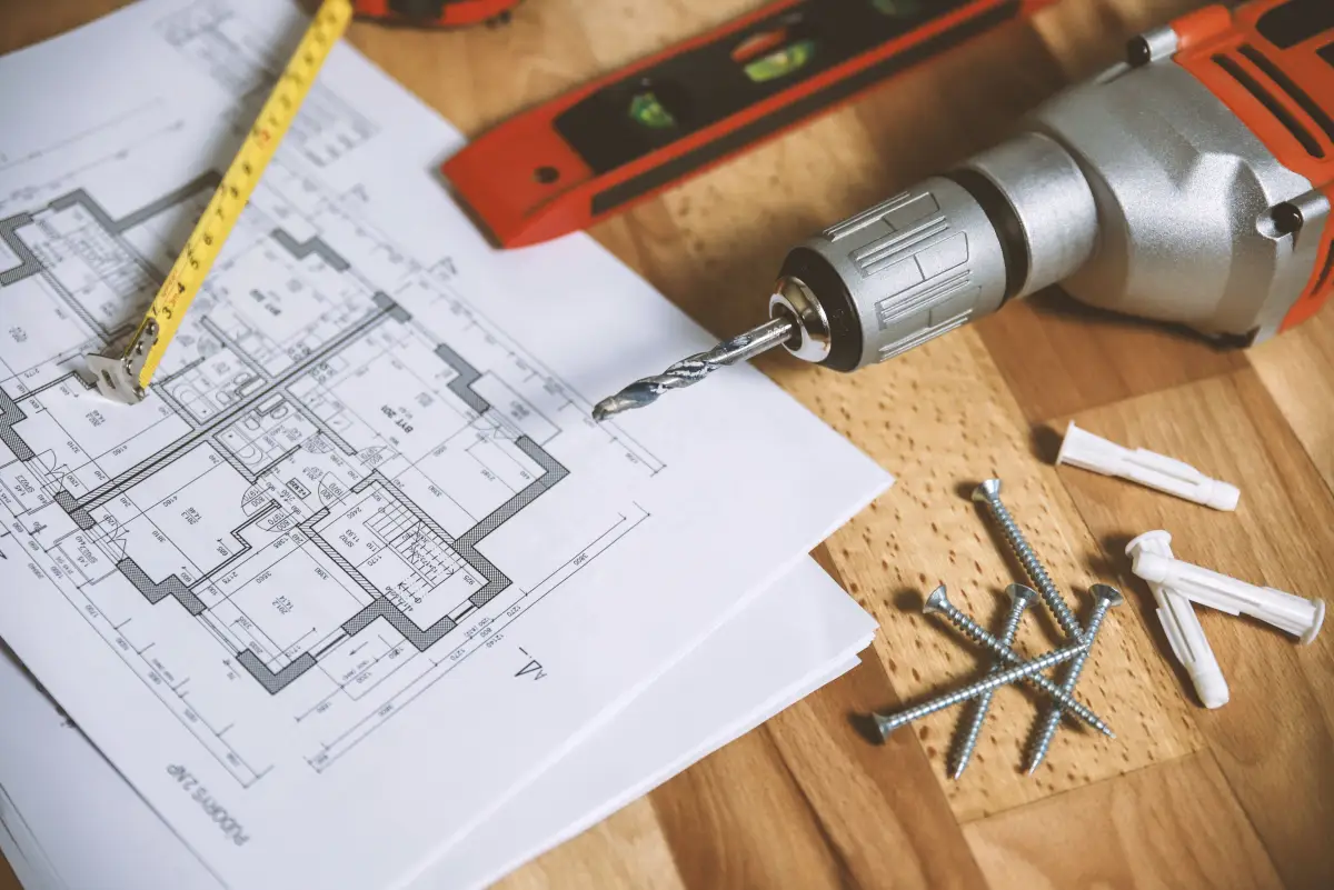 A construction drawing on a bench with a tape measure, cordless drill and screws laid across it