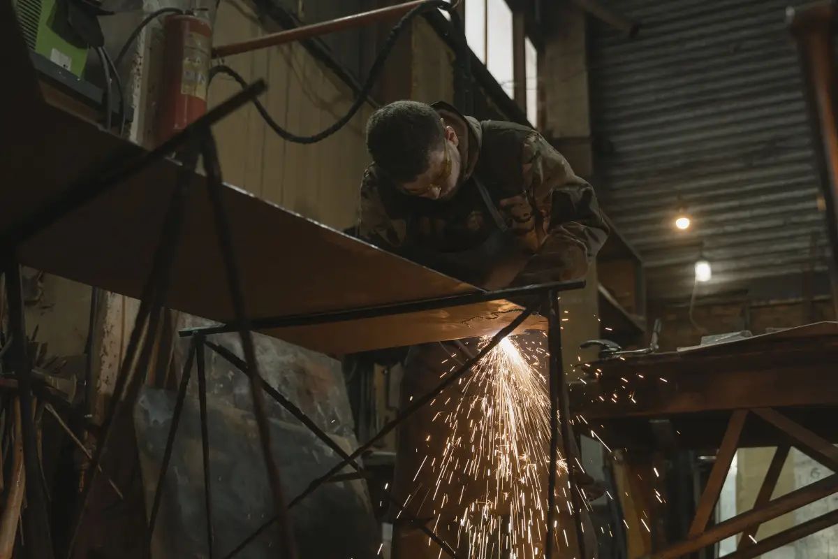 A fabricator grinding a welded steel frame in the shop, sparks coming off the joint