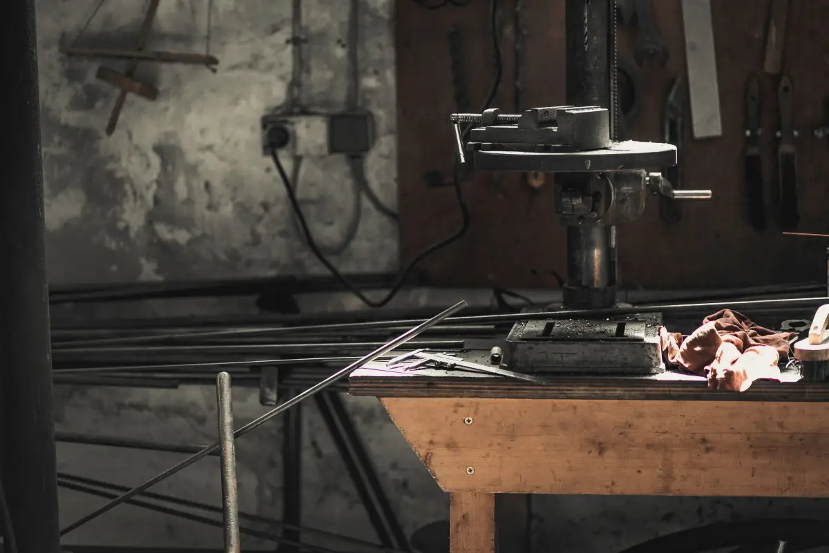 A metalwork bench with a drill press, hand tools and lengths of steel rod