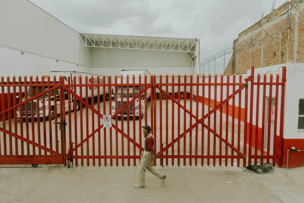 A wide red picket gate closed across an industrial facility entrance