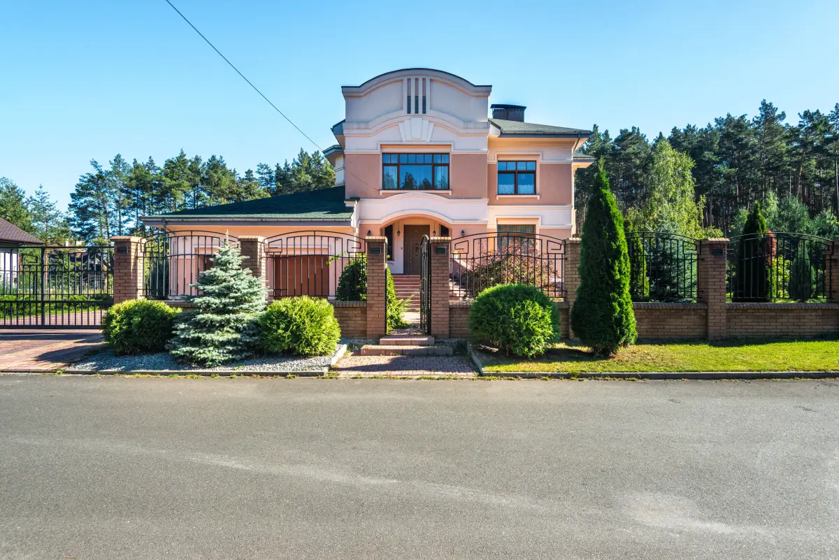 A suburban house behind a metal fence and gate set between brick pillars