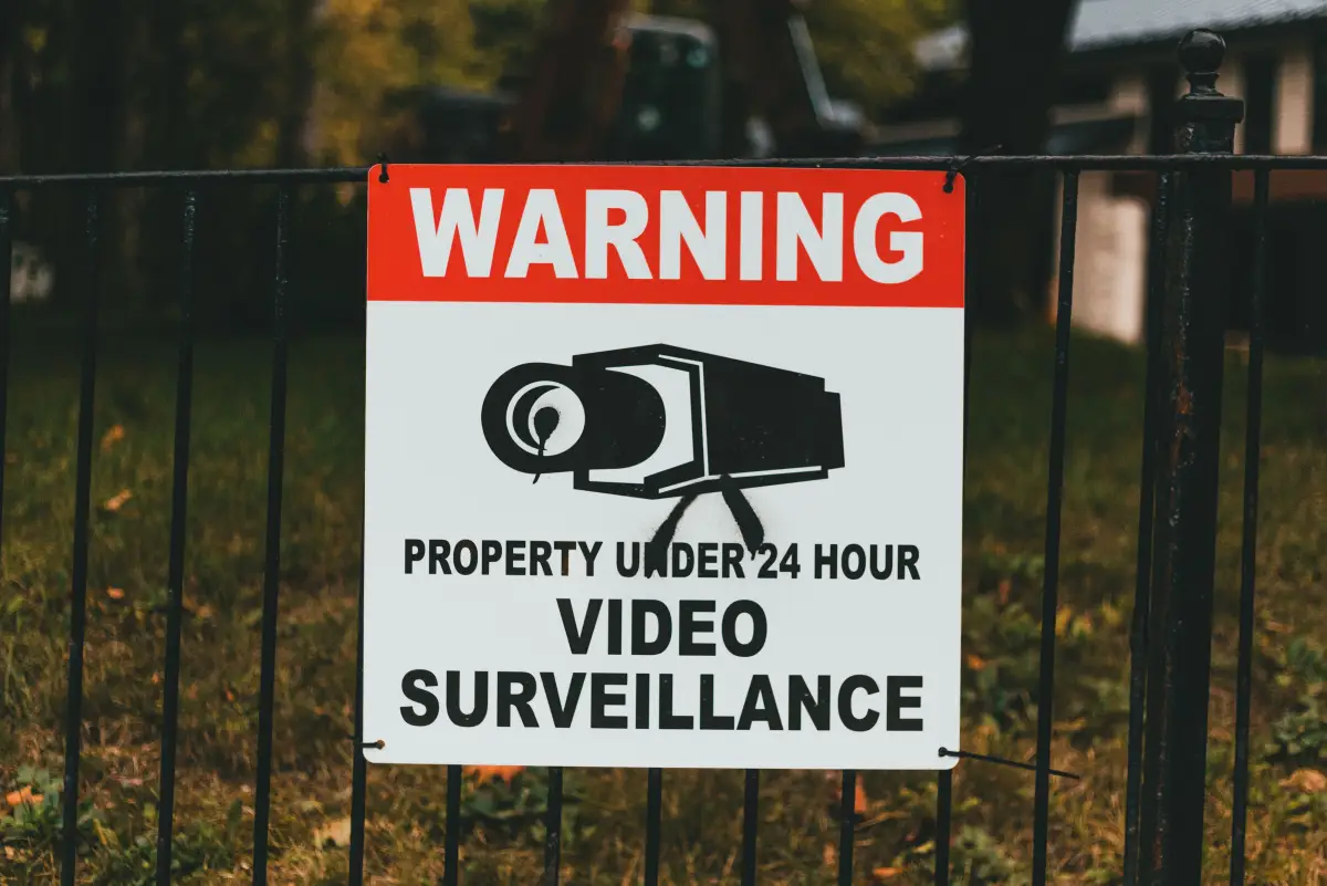 A video surveillance warning sign fixed to a black metal perimeter fence