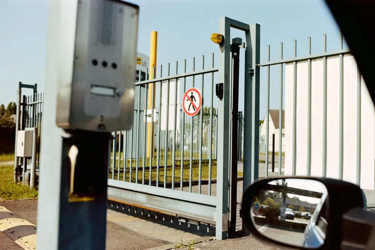An electric gate with an intercom pedestal, seen from a car window