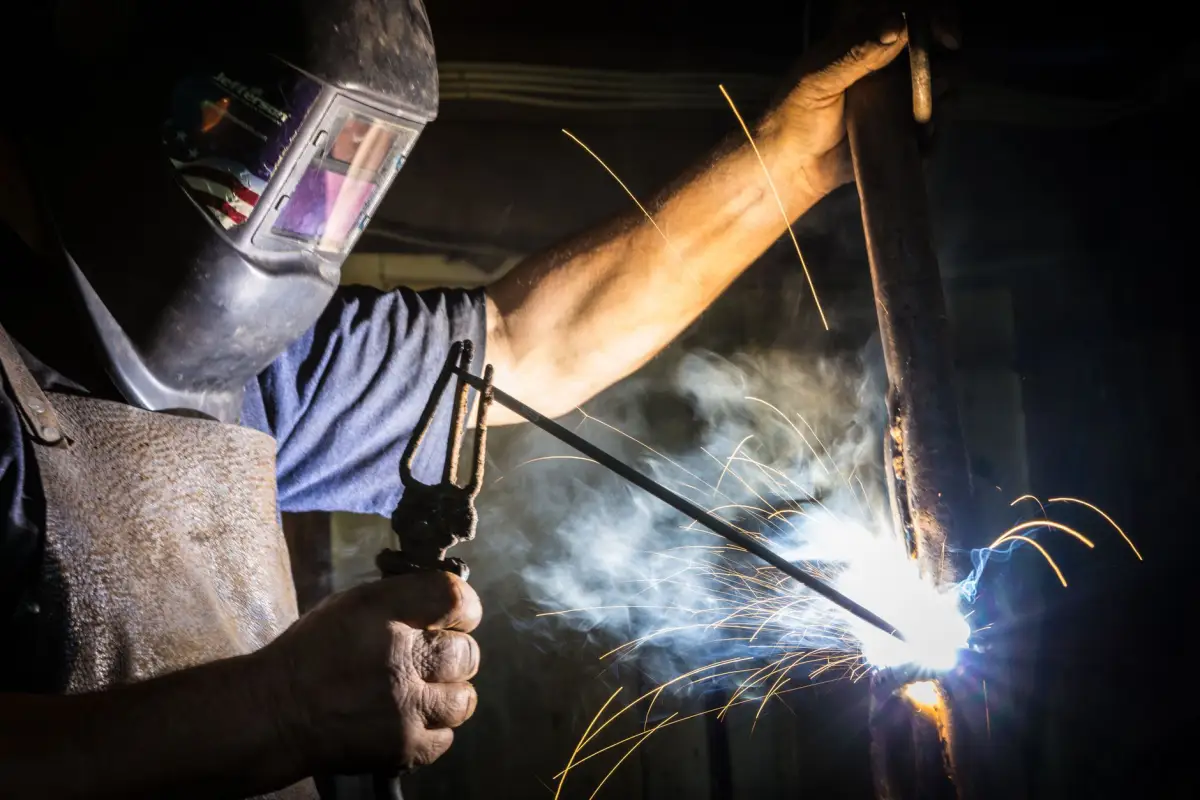 A fabricator welding a steel gate frame, sparks flying from the joint
