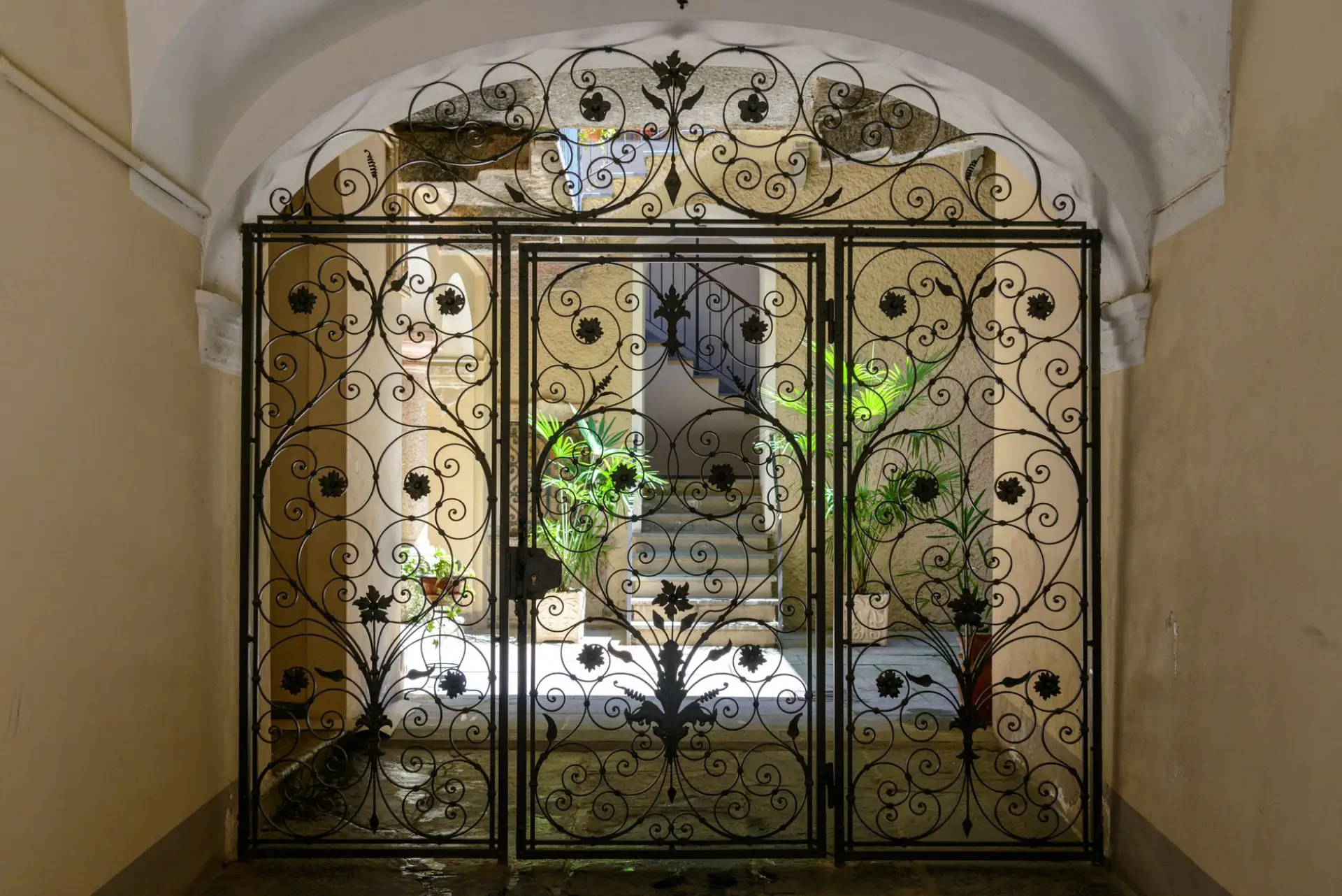 Ornamental iron gate standing open onto a sunlit walkway