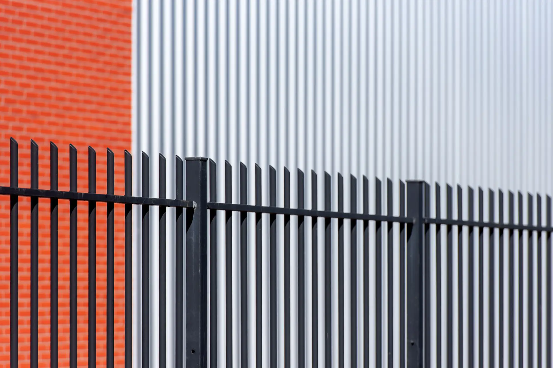A black metal security gate set into a brick and steel fence line