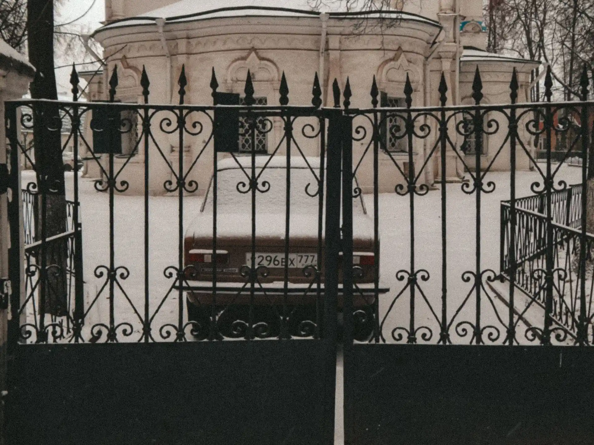 An iron swing gate open onto a snow-covered courtyard